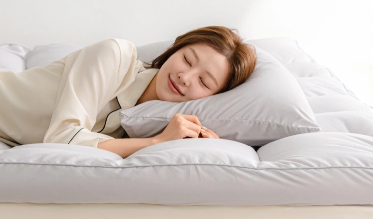 수면용품 브랜드 슬립슬러의 제품 이미지. 흰 잠옷을 입은 모델이 도톰한 흰 이불과 베개에 누워 자고 있다